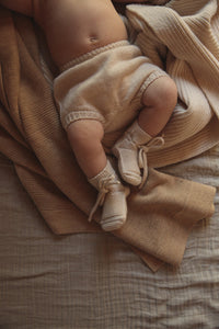 Hvid Booties Cream — baby met crèmekleurige slofjes op een stoel